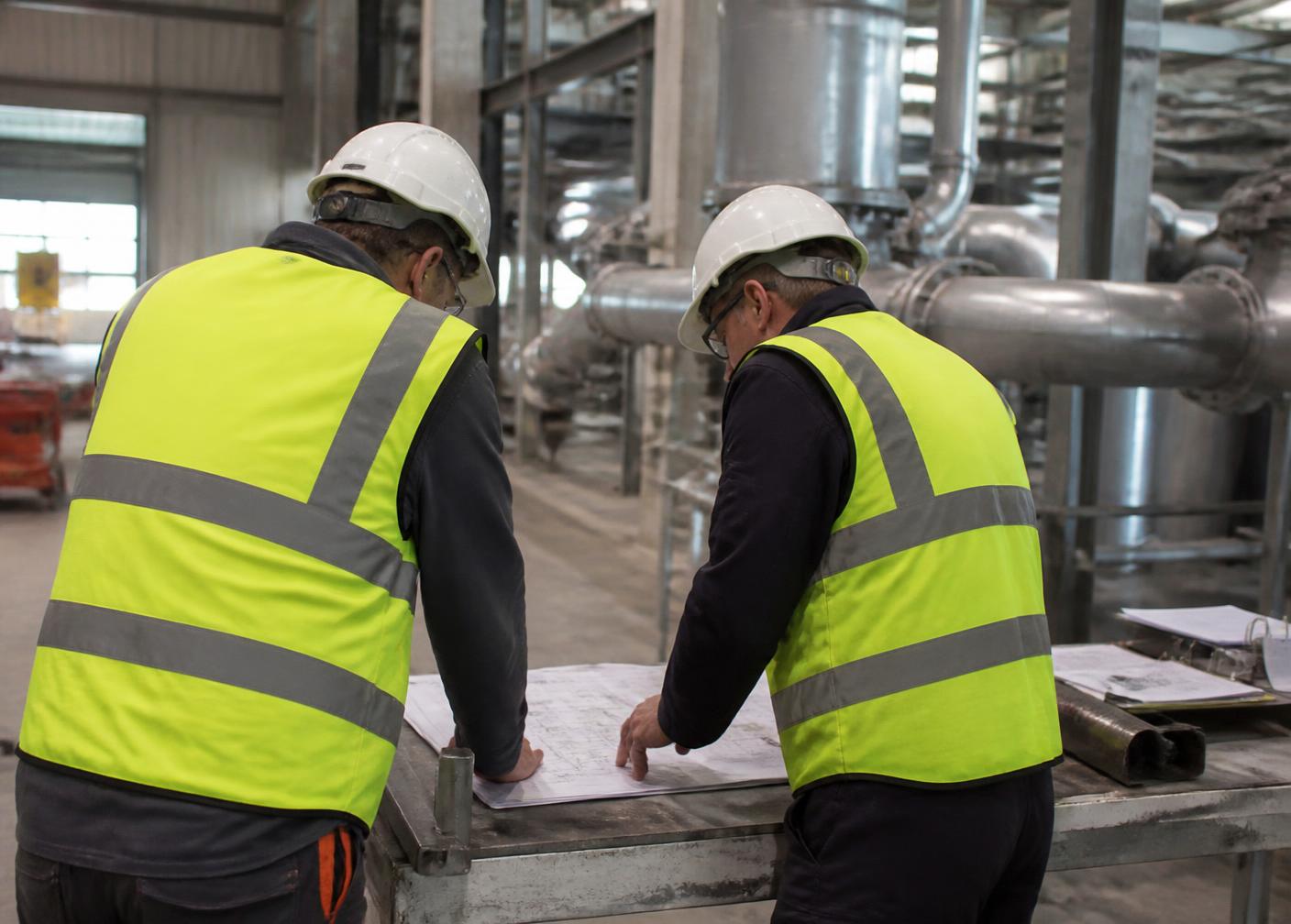 Twee technici bespreken tekeningen in een installatiehal